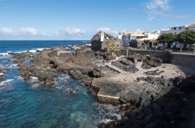 Tenerife kanarya adasının merkezinde deniz havuzu ve lav kayalıkları olan eski balıkçı köyü Garachico manzarası. Mavi gökyüzü bulutları arka planda..