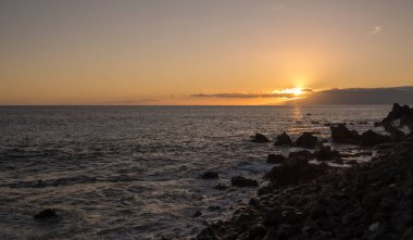 Tenerife 'nin güneyinde, Playa de San Juan, Tenerife' deki deniz kıyısında portakal rengi günbatımı siyah lav kayalarını ezen okyanus dalgalarıyla.