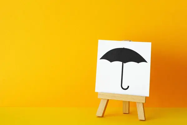 Insurance and protection concept. Black umbrella on a sign. Coverage for areas of risk, including life, health, auto, home, business insurances. Orange background with copy space