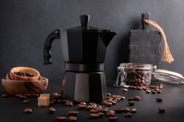 Black geyser coffee maker with roasted beans in wooden bowl and cane sugar for morning espresso on dark kitchen background