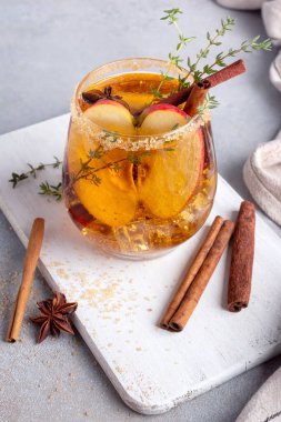 Homemade ice sweet apple cider, cocktail or mocktail with cinnamon, thyme and anise in glass for tasty and refreshing break on grey kitchen background