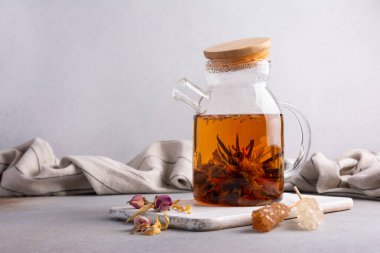 Beautiful chinese blossom or flower green tea in glass teapot with dry rose bud and cane sugar stick on grey kitchen background