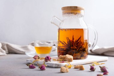 Beautiful chinese blossom or flower green tea in glass teapot and cup with dry rose bud, cane sugar on grey kitchen background