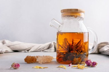 Beautiful chinese blossom or flower green tea in glass teapot with dry rose bud and cane sugar stick on grey kitchen background