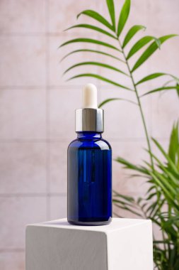Cilt kozmetik ürününün bir kopyası. Mavi eko şişesi ya da beyaz küp kaidesi üzerine doğal serum ve banyo arka planında yeşil bitki.