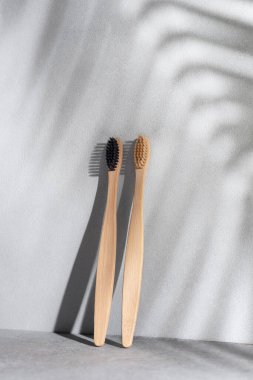 Arka planda palmiye yaprağı gölgesi olan çevre dostu bambu diş fırçaları. Sıfır atık ve plastiksiz ürün yaşamsal.