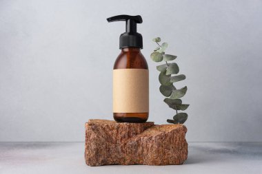 Kahverengi cam şişe, kozmetik ürünler için okaliptüs ile taşın üzerinde duruyor. Doğal organik kozmetik konsepti