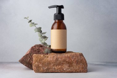 Kahverengi cam şişe, kozmetik ürünler için okaliptüs ile taşın üzerinde duruyor. Doğal organik kozmetik konsepti