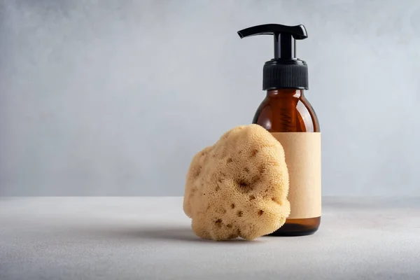 Mock up brown glass bottle and sea natural sponge on a gray background. Bath, spa treatment concept.