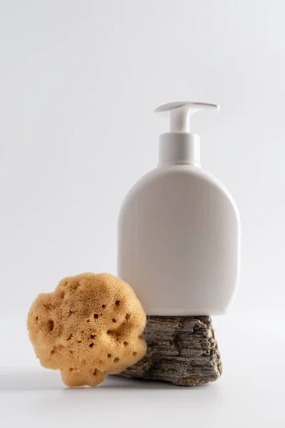 Mock up white plastic bottle and natural sea sponge on a stone podium on a gray background. Cosmetology, spa treatment concept.
