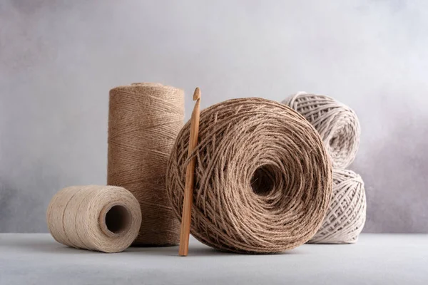 Skeins of jute rope and cotton threads with wooden crochet hook for craft and handmade on a gray background