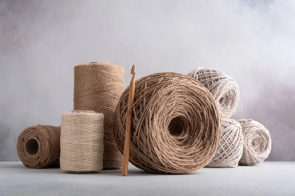 Skeins of jute rope and cotton threads with wooden crochet hook for craft and handmade on a gray background