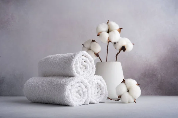 Stack of rolled white towels with cotton flower on gray background