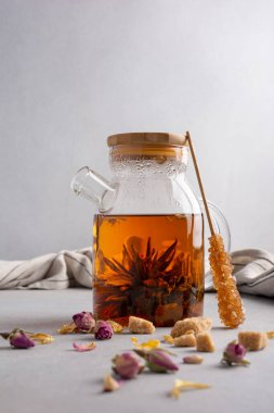 Beautiful chinese blossom or flower green tea in glass teapot with dry rose bud and cane sugar stick on grey kitchen background