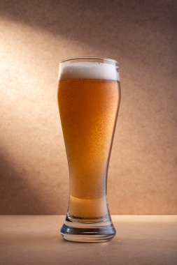 Sarı arka planda dramatik bir ışıkla bir bardak taze ve soğuk bira.