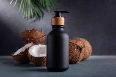 Siyah şeker şişesi ve koyu arka planda taze hindistan cevizi ve palmiye yaprakları. Hindistan cevizi yağlı organik doğal kozmetik ürünler. Markalaşma için plastik ambalaj ürünleri, modelleyin.