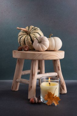 Küçük dekoratif balkabakları ve aroma mumu ahşap taburede rahat bir sonbahar evi dekoru olarak.