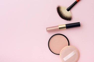 Pudra, makyaj fırçası, ruj ve sünger, pembe arka planda izole edilmiş. Kozmetik ve makyaj malzemeleri.