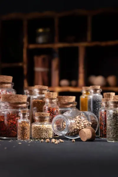 Seasoning (herbs and spices) in small bottles with cork on a dark background