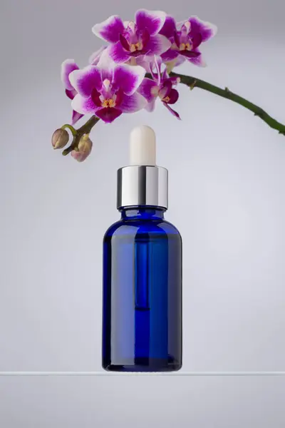 Una Elegante Botella Cuentagotas Vidrio Azul Colocada Junto Orquídeas Púrpuras Imagen de archivo