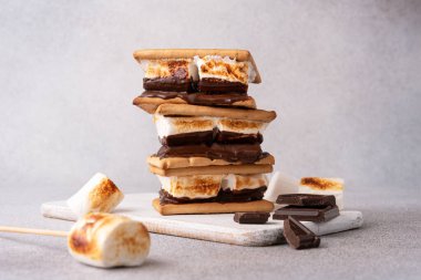 Büyük beyaz marşmelovlu taze kızartılmış börekler. Gri masada kraker ve çikolatalı leziz marshmallow sandviçi, yakın plan.. 