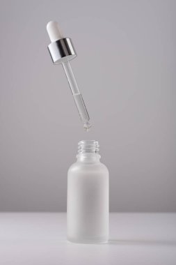 Gri arka planda pipeti olan serum şişesi. Cilt bakımı ürünleri için yakın plan buzlu cam kap..