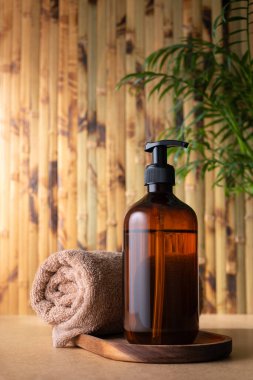 Kahverengi pompalı bir losyon şişesi ya da havluyla duş jeli, bambu duvarına karşı ahşap bir tepside oturur. Vücut bakımı ürünü, tropikal kaplıcada modelleme yapıyor. Sağlık ve bencillik kavramı.