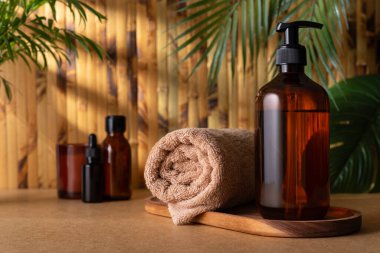 Kahverengi pompalı bir losyon şişesi ya da havluyla duş jeli, bambu duvarına karşı ahşap bir tepside oturur. Vücut bakımı ürünü, tropikal kaplıcada modelleme yapıyor. Sağlık ve bencillik kavramı.