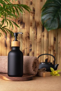 Siyah bir losyon şişesi ya da duş jeli, bambu duvarına karşı ahşap bir tepside oturur. Vücut bakımı ürünü, tropikal kaplıcada modelleme yapıyor. Sağlık ve bencillik kavramı.