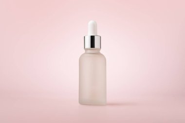 Beyaz cam damlatan serum şişesi pembe arka planda izole edilmiş.