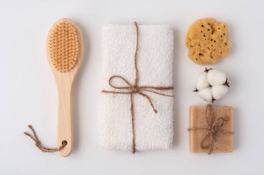 Katlanmış beyaz havlu, sabun, doğal sünger ve arka planda ahşap fırça, üst manzara. Temiz banyo ya da spa konsepti.