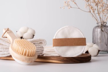 Makyaj malzemesi çıkarıcı pamuklar, ahşap banyo fırçası ve yumuşak havlular. Etik, sıfır atık kişisel bakım rutini için minimalist ve sürdürülebilir bir kavram.