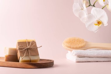 Bambu arka fırçası, el yapımı sabun çubukları ve ahşap tepside duran ve yanında narin bir orkide çiçeği bulunan doğal cilt bakımı ürünleri. Spa, sağlık ve güzellik kavramları için mükemmel..