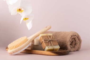 Bambu arka fırçası, el yapımı sabun çubukları ve ahşap tepside duran ve yanında narin bir orkide çiçeği bulunan doğal cilt bakımı ürünleri. Spa, sağlık ve güzellik kavramları için mükemmel..