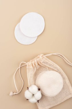 Bej bir arka planda asma ipli ağ torbası olan yeniden kullanılabilir pamuklar. Sıfır atık, çevre dostu cilt bakımı ve sürdürülebilir güzellik kavramları için mükemmel. Temiz ve minimalist estetik.