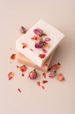 Bej arka planda kurumuş gül yaprakları olan el yapımı doğal sabunlar. Sağlık, spa, organik cilt bakımı, aromaterapi ve romantik güzellik kavramları için mükemmel..