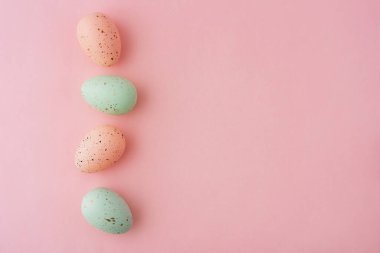 Farklı renkte dört yumurta pembe arka planda bir sırada düzenlenir. Yumurtalar benekli desenli boyanmış, Paskalya konsepti..