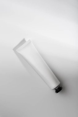 Beyaz kozmetik tüpün, parlak bir yüzeyde yumuşak gölgeli siyah kapaklı minimalist bileşimi. Markalaşma, ürün tasarımı ve cilt konsepti için ideal.