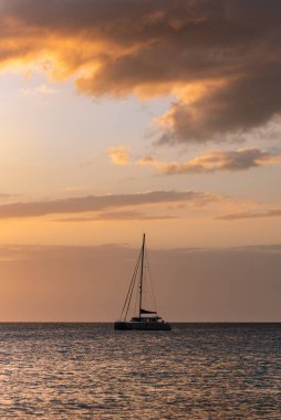 Altın bir günbatımında sakin bir okyanusta yelkenli silueti. Seyahat, rahatlama ve deniz manzarası için ideal.