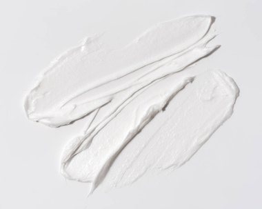 Beyaz arkaplanda yumuşak ve pürüzsüz dokunuşlarla uygulanan beyaz cilt kremi dokusu yakın plan. Güzellik, cilt bakımı, sağlık veya minimalist ürün kavramları için mükemmel..