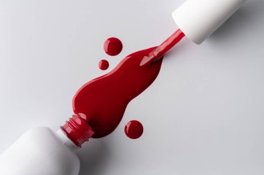 Temiz beyaz bir yüzeye parlak damlalarla dökülen kırmızı oje yakın plan. Düz doku, modern minimalizm ve canlı renk güzellik, moda veya kozmetik temalar için mükemmel..