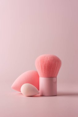 Pembe makyaj fırçası ve süngerlerin minimalist fotoğrafı kozmetik uygulamaları için zarif güzellik aletleri. Reklam, güzellik veya cilt temaları için mükemmel, yumuşak dokular ve modern tasarım sergileniyor.