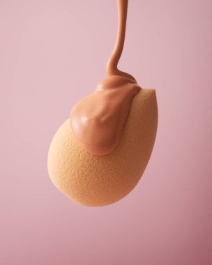 Yumuşak pembe bir zemine dökülen sıvı temeli olan bir makyaj süngeri blenderi. Güzellik, kozmetik, cilt bakımı ve profesyonel makyaj temaları için mükemmel..