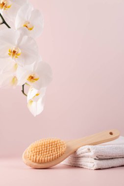 Beyaz orkide çiçekleri ve pastel pembe arka planda havlularla doğal kıllı vücut fırçası. Minimalist kaplıca ve kişisel bakım kavramı, doğal güzellik ve refahı vurguluyor..