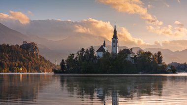 Gün doğumunda dağlarla çevrili ada ve kilise manzaralı Bled Gölü manzarası. Suda yansımaları olan sakin yaz manzarası.