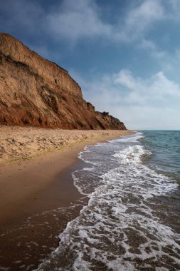 Sahil uçurumları ve açık mavi gökyüzünün altında köpüklü deniz dalgaları olan vahşi bir sahil manzarası. Doğal dokunulmamış kıyı şeridi, seyahat, doğa ve jeoloji kavramları için idealdir. Karadeniz, Ukrayna.