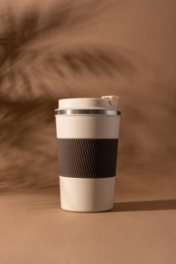 Yeniden kullanılabilir kahve fincanı, doğal gölgeli sıcak bej arka plan modeli. Markalaşma, paketleme, eko tasarım veya reklam için minimalist ürün şablonu. 