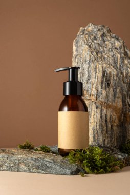 Minimum kehribar kozmetik şişe modeli, pompalı ve üzerinde taş ve yosun arkaplan etiketi olan boş bir kraft etiketi. Organik cilt bakımı, ekolojik ürün markalaşması ya da doğal güzellik sunumları için mükemmel..