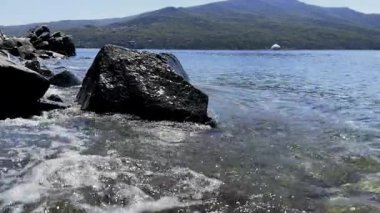 Sörf dalgaları köpüğe dönüşür ve sahildeki büyük taşlara sıçrar. Su kaynıyor, kayaların üzerinde yuvarlanıyor ve denize geri dönüyor. Suyun gücünün peyzajı ve taşın dayanıklılığı. Elementlerin kavşağında.