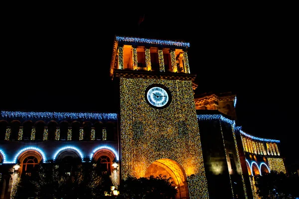 stock image Glowing building tower and huge clock. Beautiful building architecture. The walls of the building are covered with lights